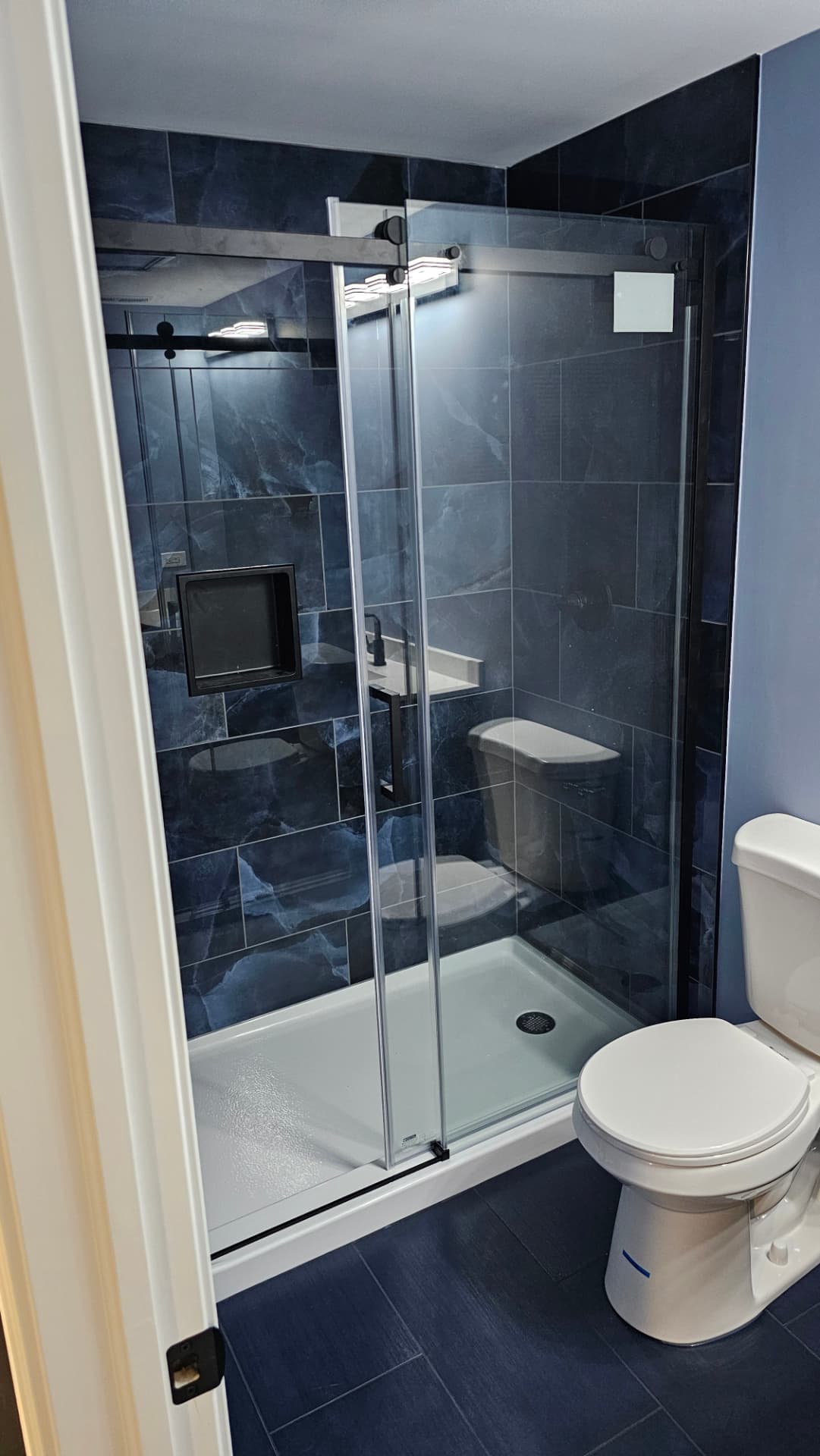 Shower finished in large navy marble-look tile with a black frameless sliding glass door and inset niche