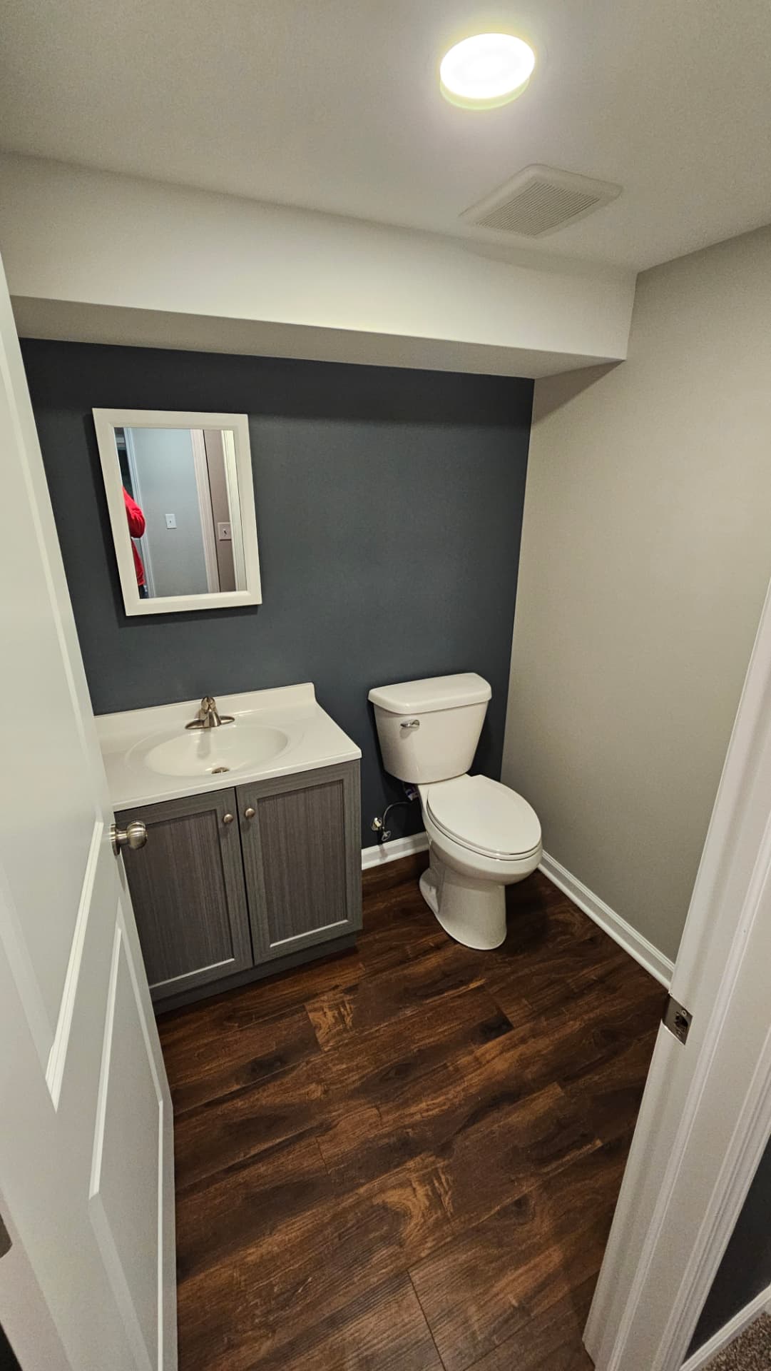 Half bath with a navy accent wall, grey vanity and dark plank flooring