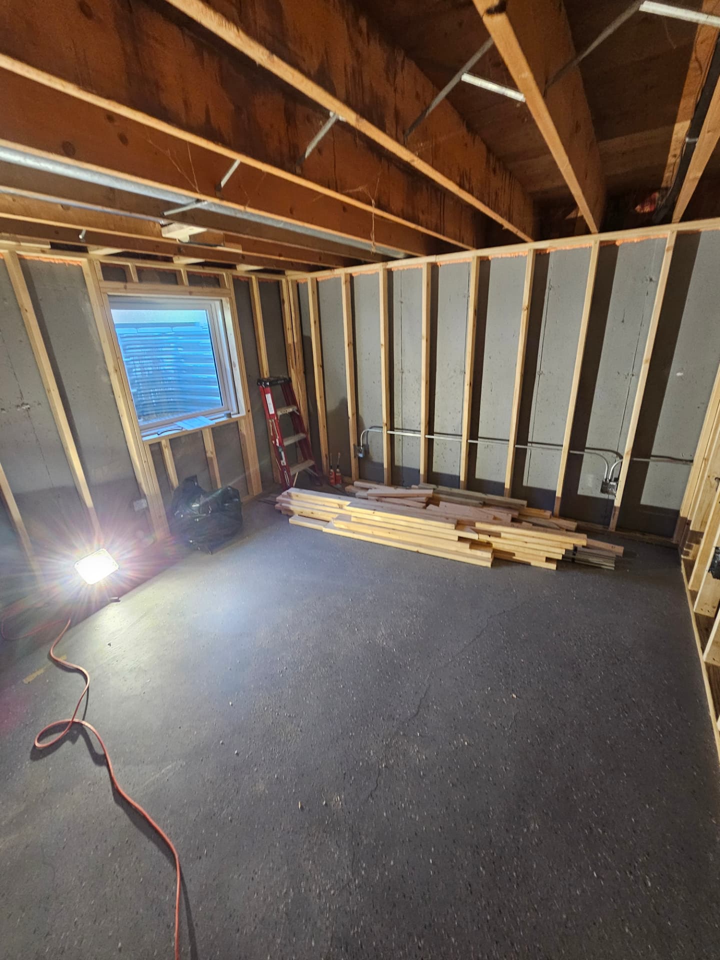 Basement bedroom under construction with new stud framing against the foundation wall